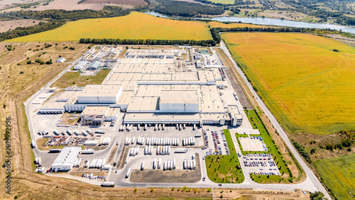 Wide aerial panorama of industrial complex in rural landscape. Panoramic aerial view of a large logistics hub surrounded by agricultural fields, a river, and forest.