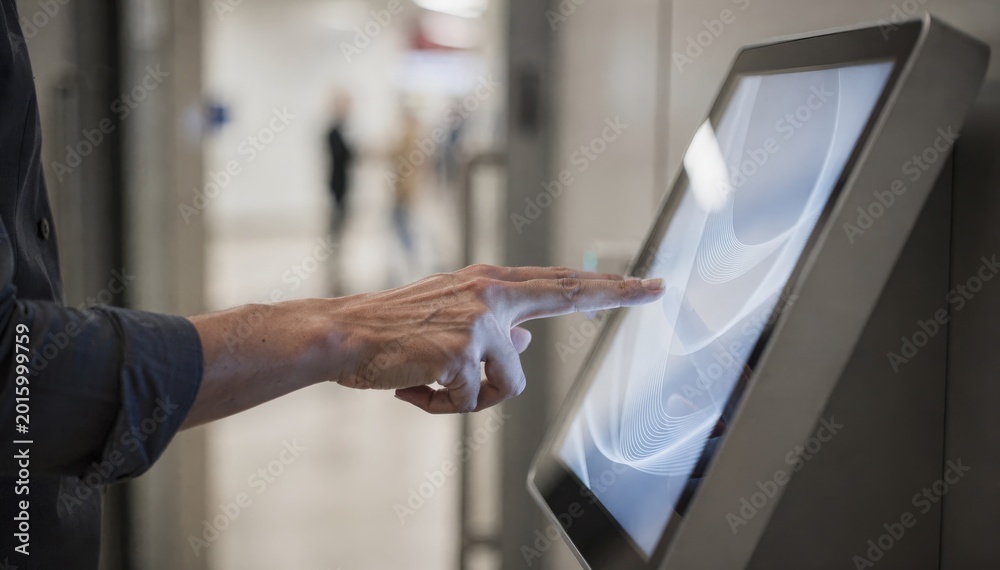 Obraz premium Medium shot showing a user navigating a compact digital touchscreen kiosk near a doorway with clear focus on the hand and screen imagery background subtly blurred.