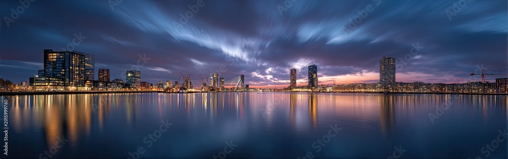 Fototapeta premium Panoramic view of a modern city skyline at dusk with vibrant lights reflecting on the water.
