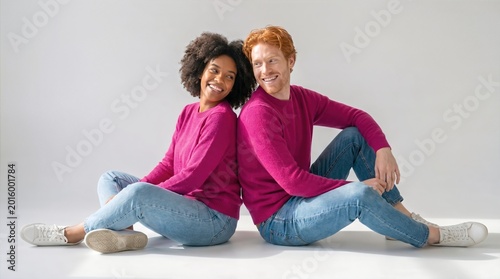 African American woman and caucasian man with red hair sitting back-to-back on floor smiling happily. Joyful friendship and modern relationship concept