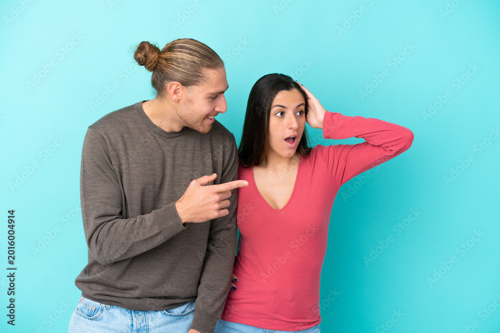 Obraz premium Young caucasian couple isolated on blue background pointing finger to the side with a surprised face