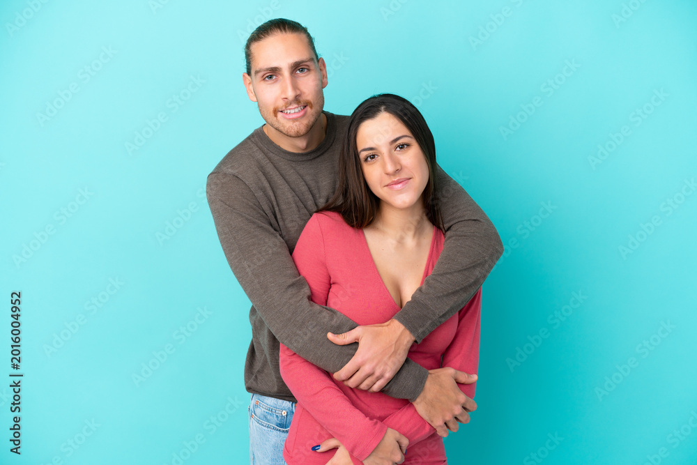Fototapeta premium Young caucasian couple isolated on blue background hugging