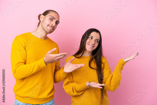 Tablou pe pânză Young caucasian couple isolated on pink background extending hands to the side f