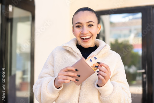 Young moroccan girl  at outdoors holding wallet with money with happy expression
