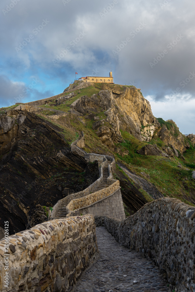 Fototapeta premium Stone pathway leading to San Juan de Gaztelugatxe under dramatic sky