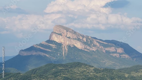 Iconic Pena Montanesa rock formation in the Spanish Pyrenees. Majestic mountain landscape with green forests and a cloudy blue sky