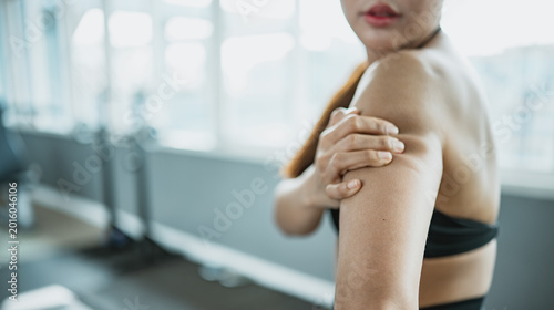 Photos Asian fitness woman holding sore upper arm after exercise in gym