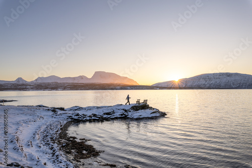 Person walking to the bench over malangen fjord at sunrise, surrounded by peaceful Arctic winter scenery