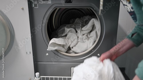 Woman loading clean white laundry into tumble dryer at home laundry room