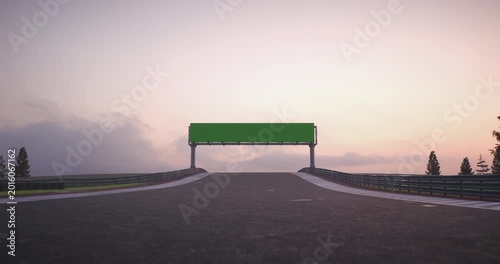Race cars drive toward a billboard on a racing track at sunset, wide angle view with asphalt, horizon, clouds and forest landscape