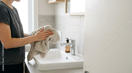 Woman drying hands with a towel in a modern bathroom.