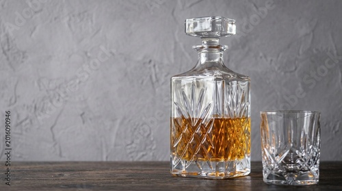 Crystal decanter and glass filled with amber whiskey on a wooden table, elegant drinkware