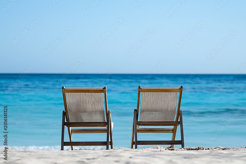 Fototapeta premium Two empty beach chairs facing the ocean on a sunny day inviting relaxation coastal leisure and peaceful vacation moments.