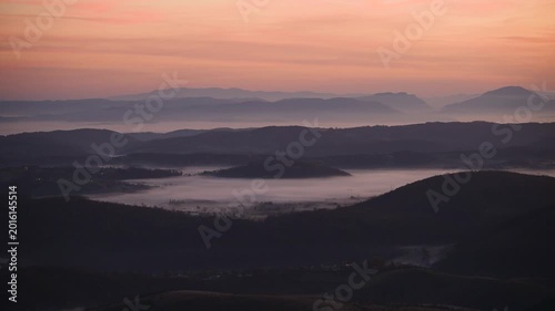 View from mountain Zlatibor in southern Serbia, hilly landscape with valleys filled with morning fog and hill layers in background, clouds are orange color at dawn