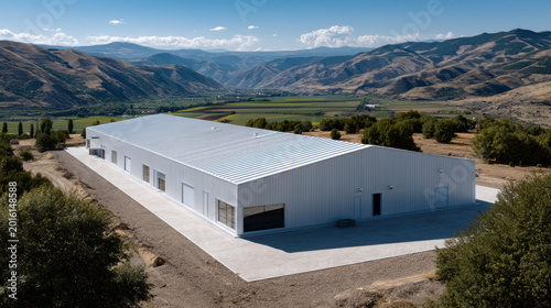 Large industrial building with metal roof, mountain landscape, blue sky, rural area, modern warehouse, spacious facility, sunny day