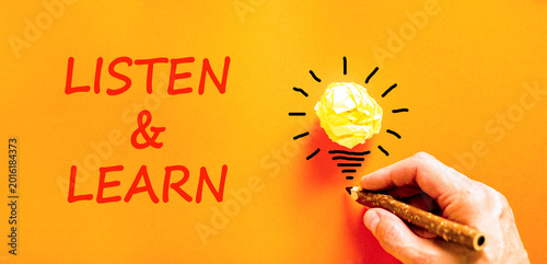 Listen and learn symbol. Concept words Listen and learn on beautiful orange paper. Beautiful orange background. Light bulb icon. Businessman hand. Business listen and learn support concept. Copy space