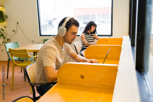 Photos Young man wearing headphones and concentrating on laptop, working remotely in a