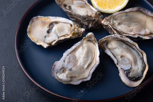 Moari oysters, live, fresh, opened. Served with half a lemon. Blue plate, black background. Selective focus, close-up.