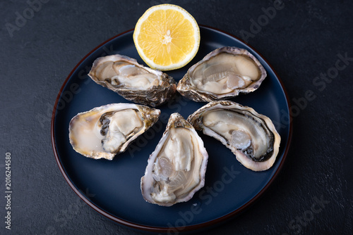 Moari oysters, live, fresh, opened. Served with half a lemon. Blue plate, black background. Selective focus, close-up.