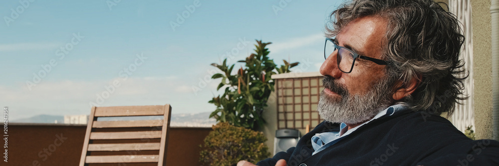 Naklejka premium Middle-aged man enjoying sunny weather on the balcony. Panoramic