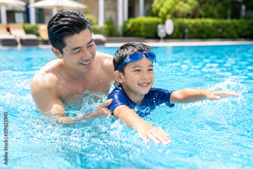 Father teaching young son swimming in outdoor pool
