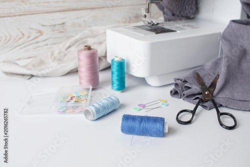Sewing supplies on a white table with a sewing machine in the background. Sewing machine with fabric and sewing accessories on a white table.
