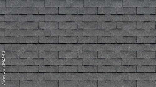 A close-up image of gray asphalt shingles arranged in a brick pattern. The shingles create a textured, dark gray surface.