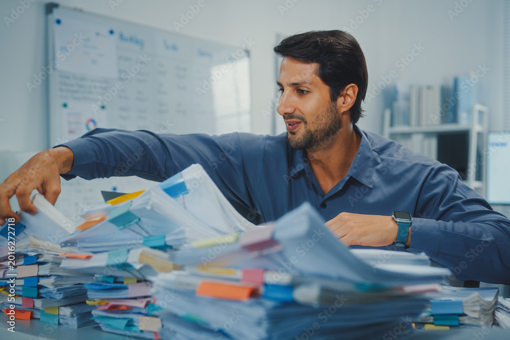 Ταπετσαρία Overworked young Latin businessman reading document in large stack of paperwork files at office desk