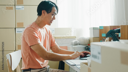 Foto Young Asia male entrepreneur small business confirm purchase order from customer parcel barcode tracking number on laptop computer check inventory product ready shipping at small online retail shop