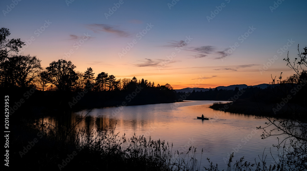 Obraz premium A solitary person kayaking on a calm river during a vibrant sunset.
