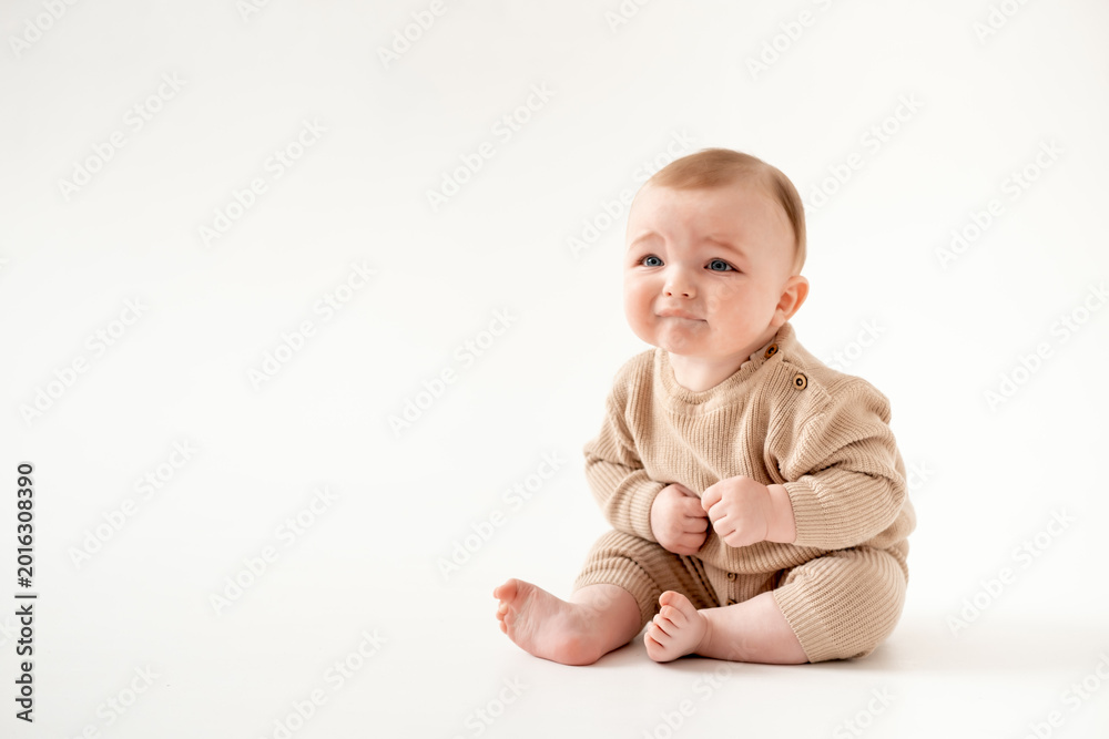 Fototapeta premium a crying baby on an isolated white background, a small boy crying or calling for his mother in a brown knitted suit