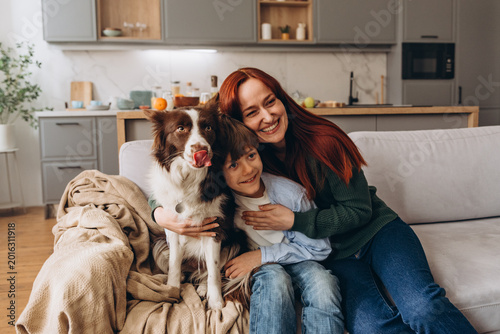 Foto Woman hugs boy and dog during close moment while dog licks nose on sofa