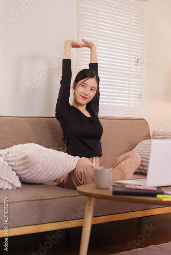 Asian women stretching arms relaxing on sofa at home living room working from home remote work wellness lifestyle enjoying break with laptop computer and