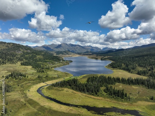 Aerial drone captures serene mountain lake surrounded by lush green valleys and dense forests under dramatic cloud-filled skies