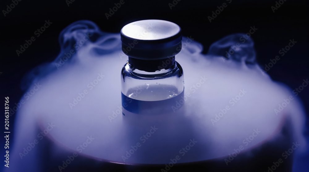 Obraz premium Glass vial with blue label sits in dense fog from dry ice. Liquid inside vial appears clear and stable. Cryogenic preservation and medical research concept.