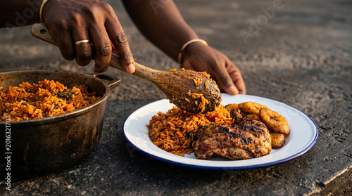 Person serving a plate of jollof rice with grilled chicken and plantains