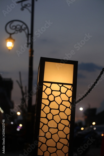 Artistic urban lights stand out in the foreground, with soft bokeh from the illuminated lights behind them.