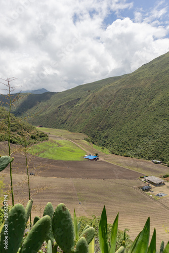 Drone aerial view of a rural farm surrounded by lush green mountains in Tenerife Valley, Colombia. Agricultural fields with neatly planted crops, countryside houses, rolling hills, and natural landsca