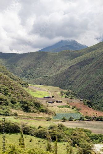 Drone aerial view of a rural farm surrounded by lush green mountains in Tenerife Valley, Colombia. Agricultural fields with neatly planted crops, countryside houses, rolling hills, and natural landsca