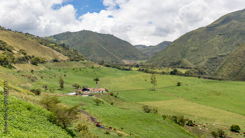 Drone aerial view of a rural farm surrounded by lush green mountains in Tenerife Valley, Colombia. Agricultural fields with neatly planted crops, countryside houses, rolling hills, and natural landsca