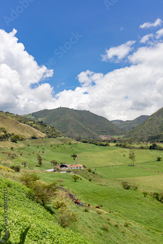 Drone aerial view of a rural farm surrounded by lush green mountains in Tenerife Valley, Colombia. Agricultural fields with neatly planted crops, countryside houses, rolling hills, and natural landsca