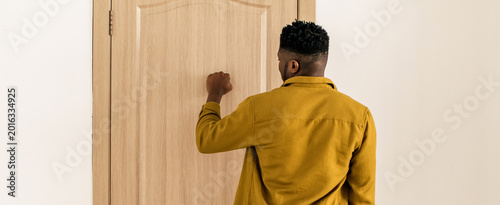 Cuadro en lienzo A man stands with his back to the camera and knocks on a plain wooden door