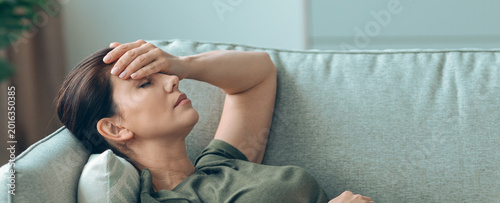 Foto Woman lies down on couch with her eyes closed, touching her forehead with one hand