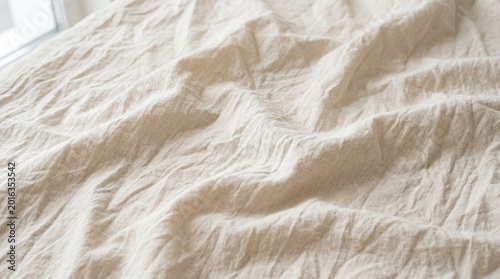 Textured close-up of a soft, light beige fabric, gently rumpled with natural creases and folds, creating an inviting and comfortable aesthetic. Ideal for backgrounds and design