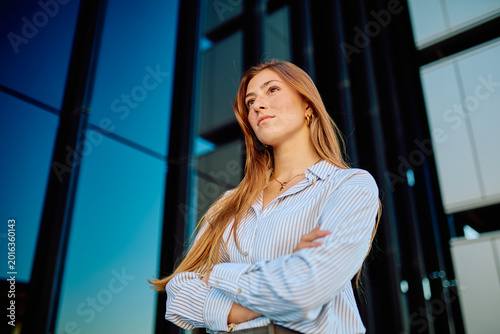Obraz na płótnie Confident young businesswoman standing with crossed arms against a modern buildi
