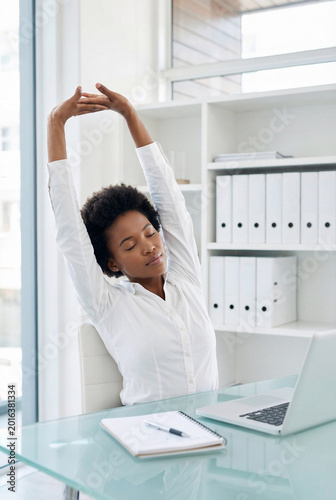 Businesswoman Stretching at Desk During Work Break in Modern Bright Office