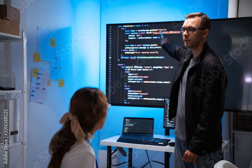 Software developers discussing code on large screen in office