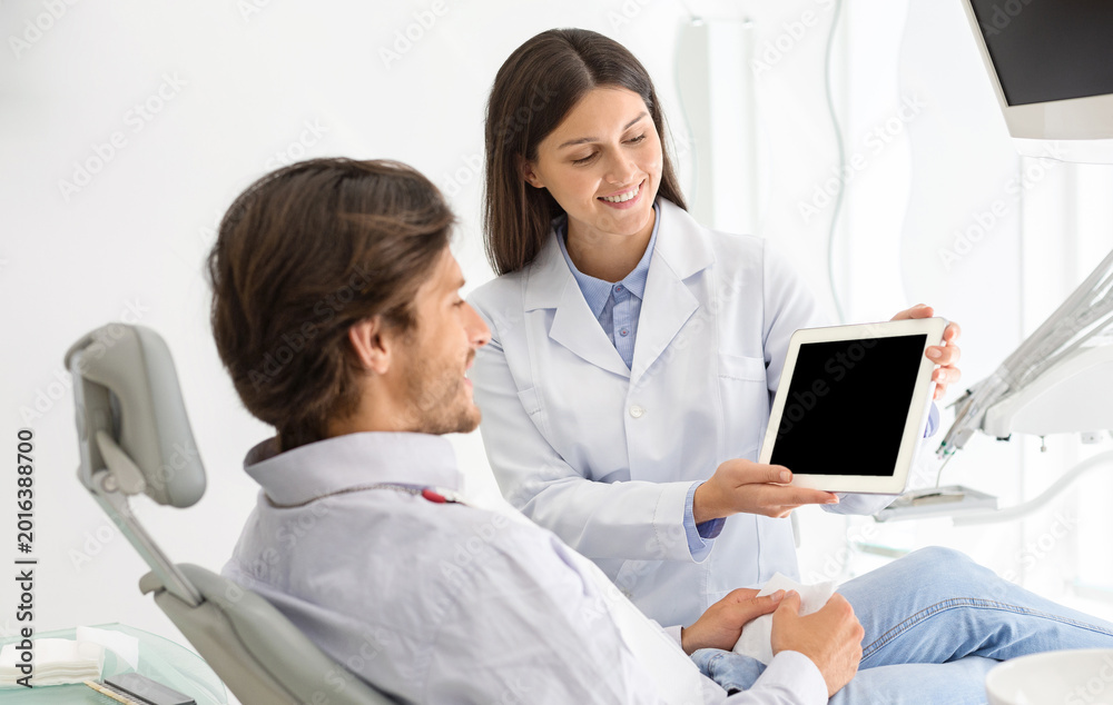 Obraz premium Woman dentist doctor showing patient empty digital tablet screen, modern technologies in healthcare