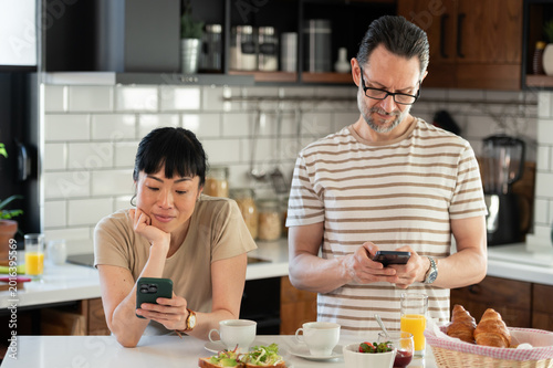 Couple using smartphones during breakfast in a modern kitchen, illustrating digital lifestyle, social media habits, online communication and technology in everyday home life