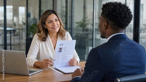 Friendly female human resources manager reviewing resume and interviewing male job applicant in a bright modern office, career recruitment and professional employment concept.